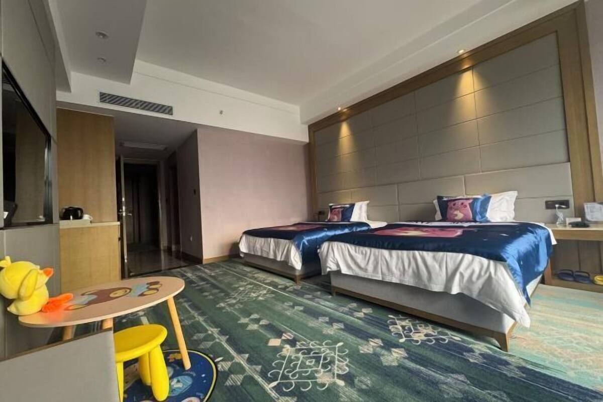 A hotel room with two beds, a small table with a chair, and a large mirror.