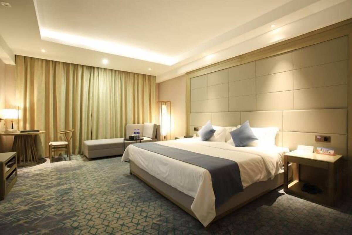A hotel room with a large bed, a desk, a chair, a sofa, and a bedside table.