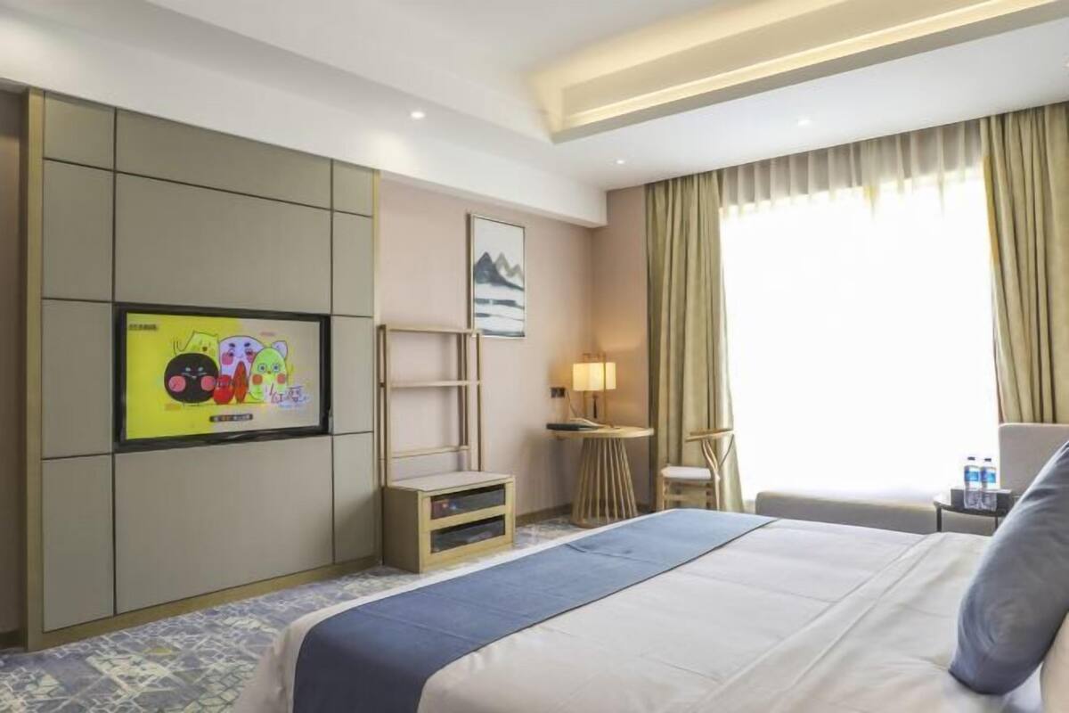 A hotel room with a bed, a TV mounted on the wall, a small table with a lamp, and a chair.