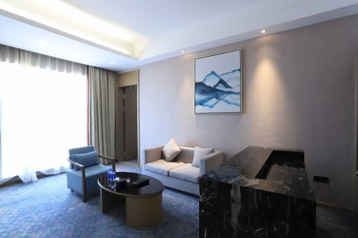 A modern hotel room with a sofa, armchair, coffee table, and a marble fireplace.