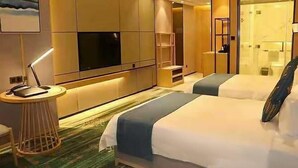 A hotel room with two beds, a TV, a desk, and a small side table.