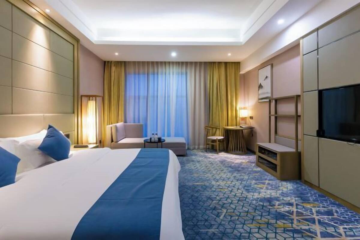 A hotel room with a large bed, a desk, a chair, a TV, and a window with curtains.