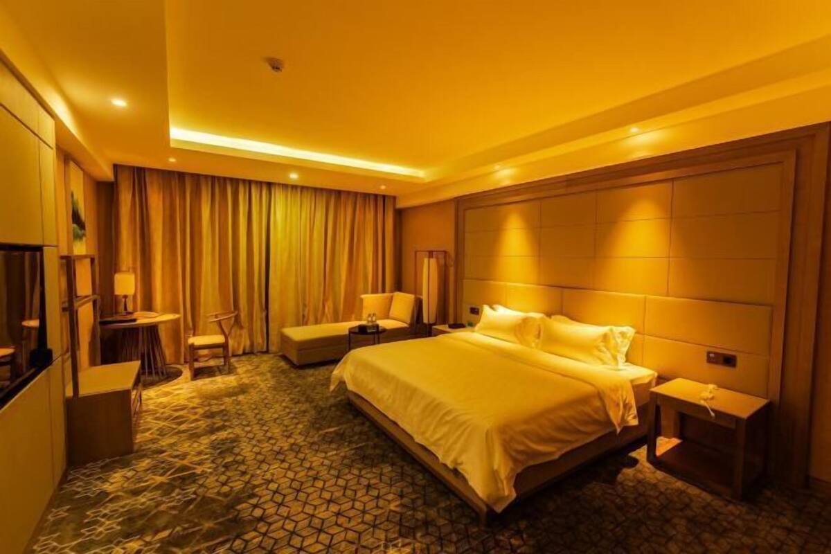 A hotel room with a large bed, a desk, a chair, a small table, and a TV.