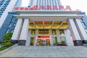 A hotel entrance with a large sign, steps leading up to it, and tall buildings in the background. - Yuda International Hotel (Wuxuan)