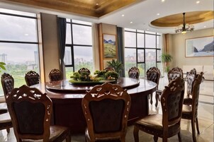 Un comedor con una mesa redonda y sillas, ventanas amplias con vistas a la ciudad y una araña.