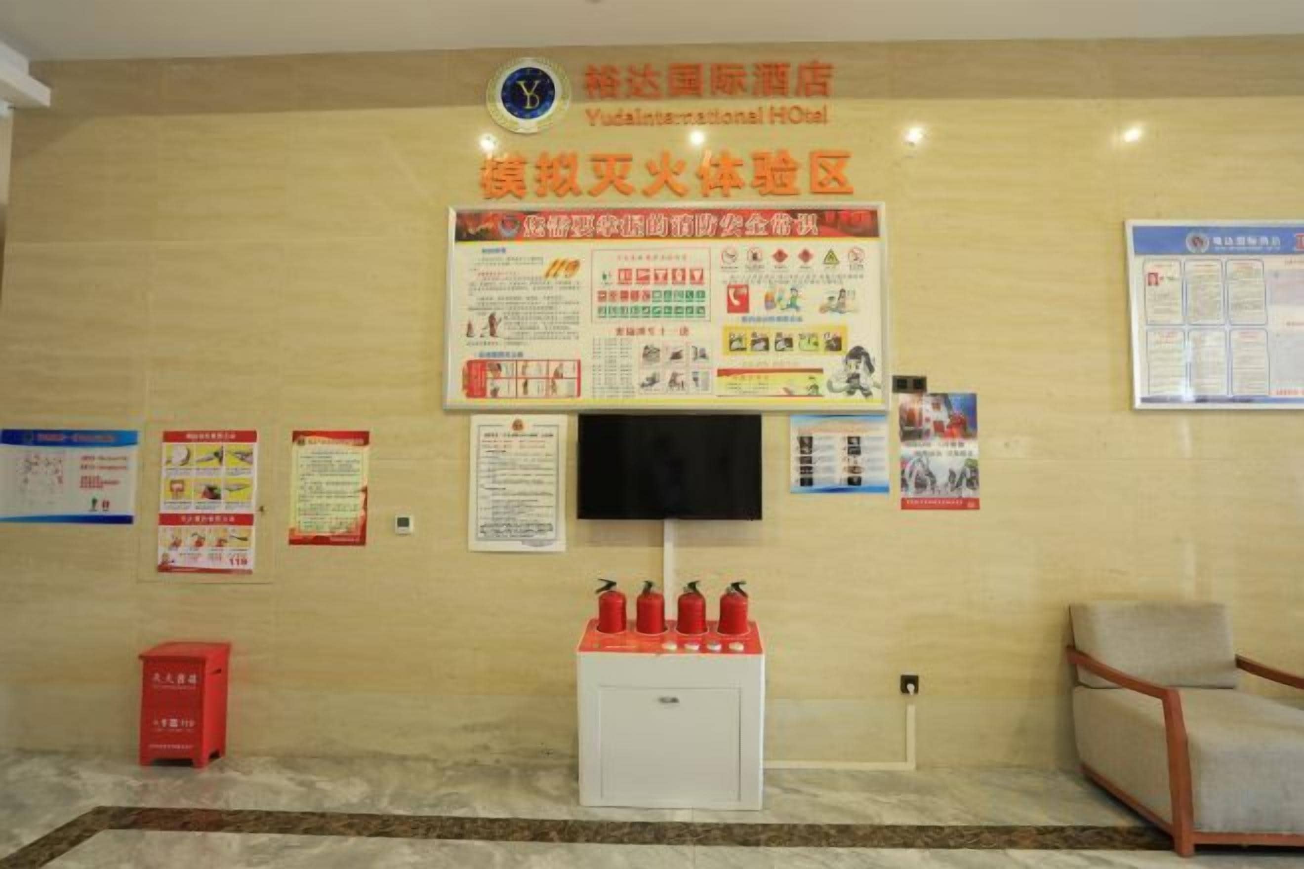 A reception area with a mounted television, informational posters, a fire extinguisher, and a seating area.