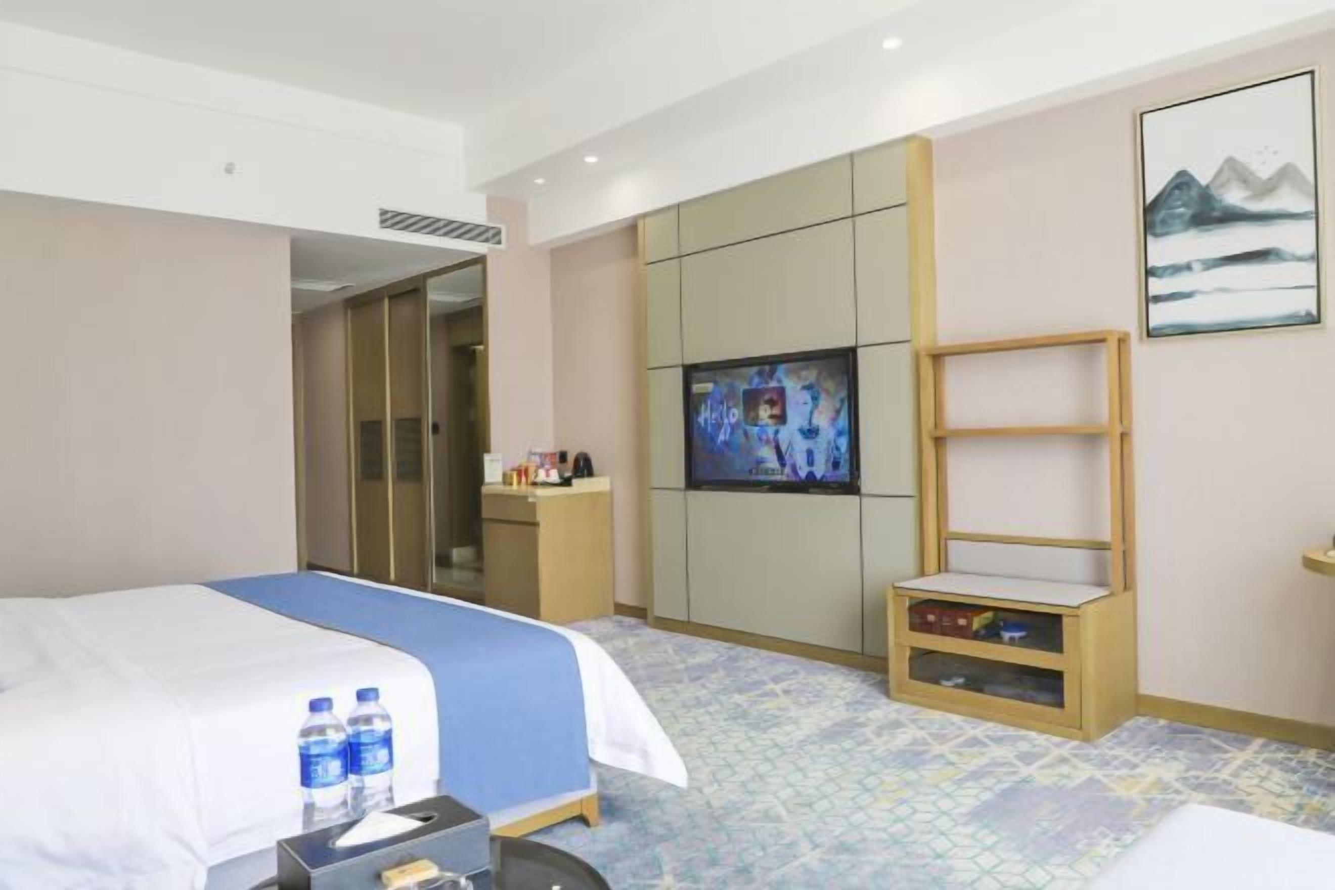 A hotel room with a bed, a television, a desk, and a shelf.