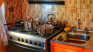 Een kleine keuken met houten kastjes, een magnetron, een fornuis met pannen en een spoelbak.