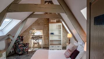 A bedroom with a sloped ceiling, a bed, a desk, and a chair.