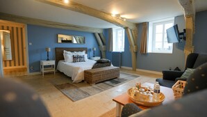 A bedroom with a bed, bedside tables, a wicker bench, a sofa, and a tray with glasses and bottles.
