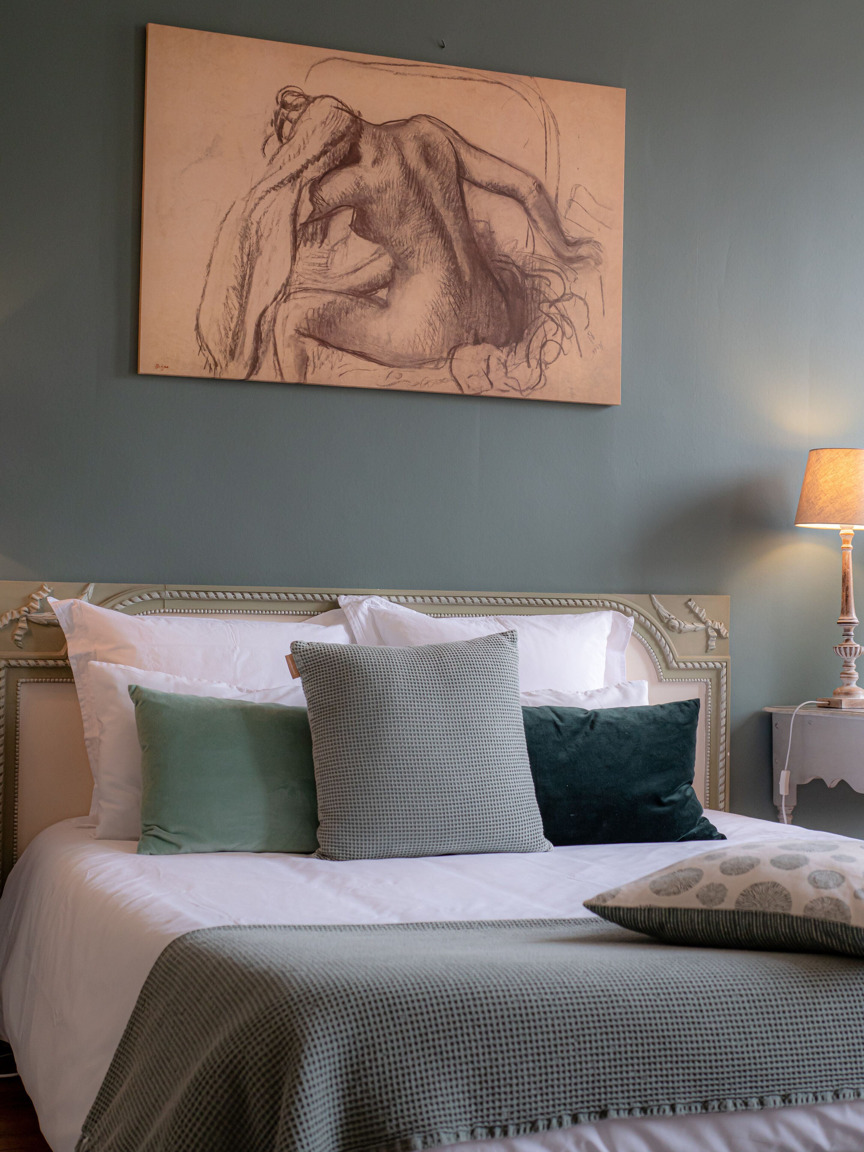 A bedroom with a bed, pillows, a lamp, and a wall art piece.