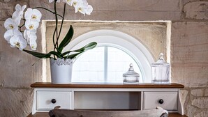 A wooden desk with a white drawer unit, a potted orchid, and two glass containers on the windowsill.