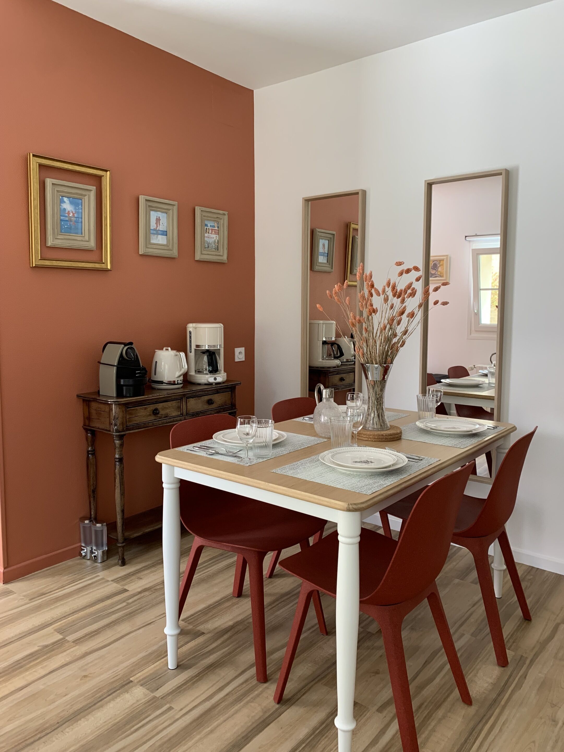 A dining area with a wooden table set for four, red chairs, and a coffee station with a kettle and coffee maker.