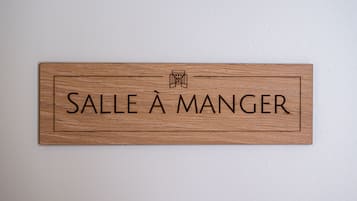 Et træskilt med teksten "SALLE À MANGER" på en hvid væg.