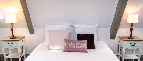 A neatly made bed with a white comforter and two pillows, flanked by two bedside tables with lamps and a white chair.