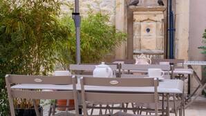 Outdoor seating with tables and chairs, a red umbrella, and a stone wall with a door and a bird perched on it.
