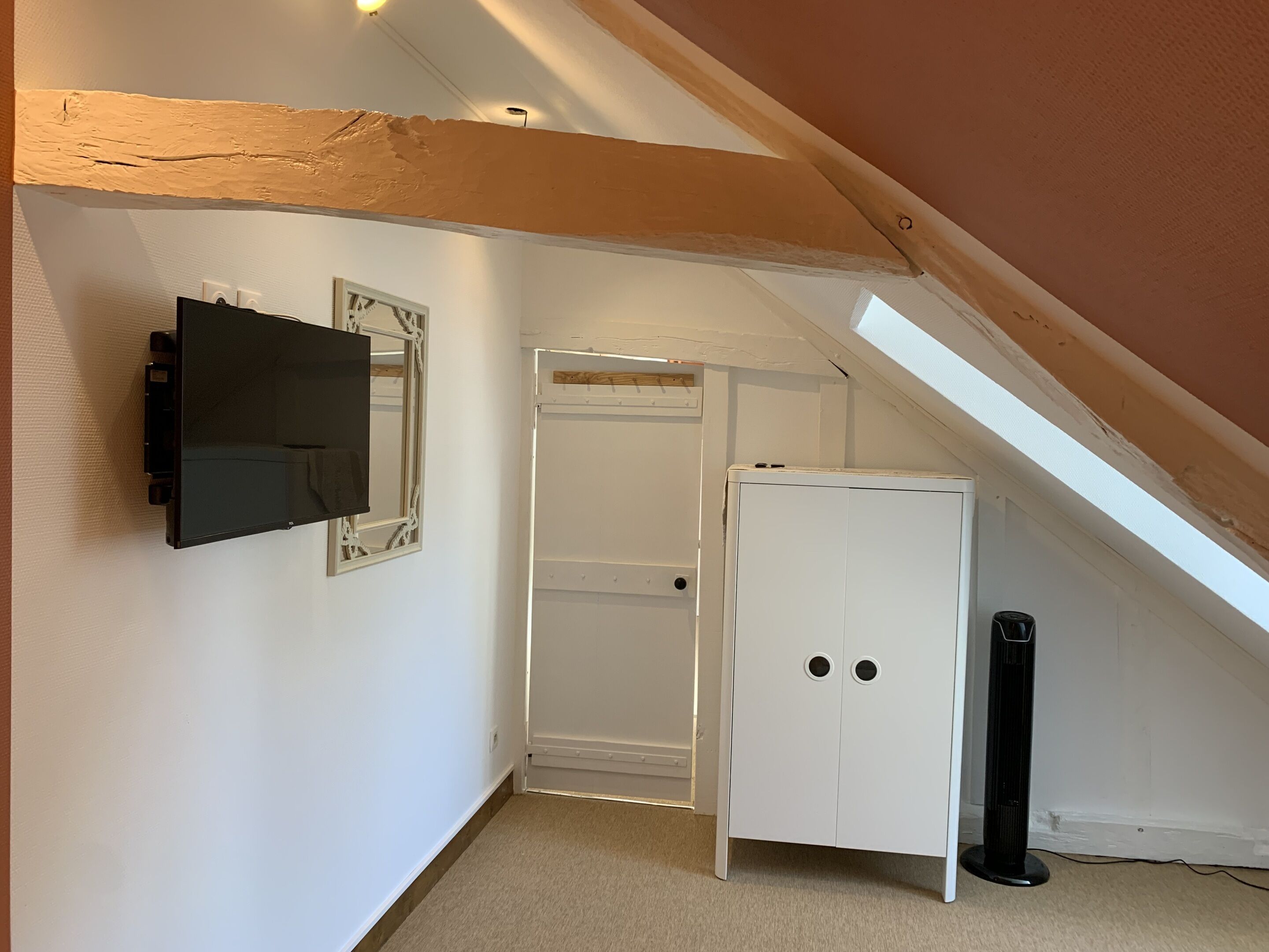A room with a white wardrobe, a black standing heater, and a mounted TV.
