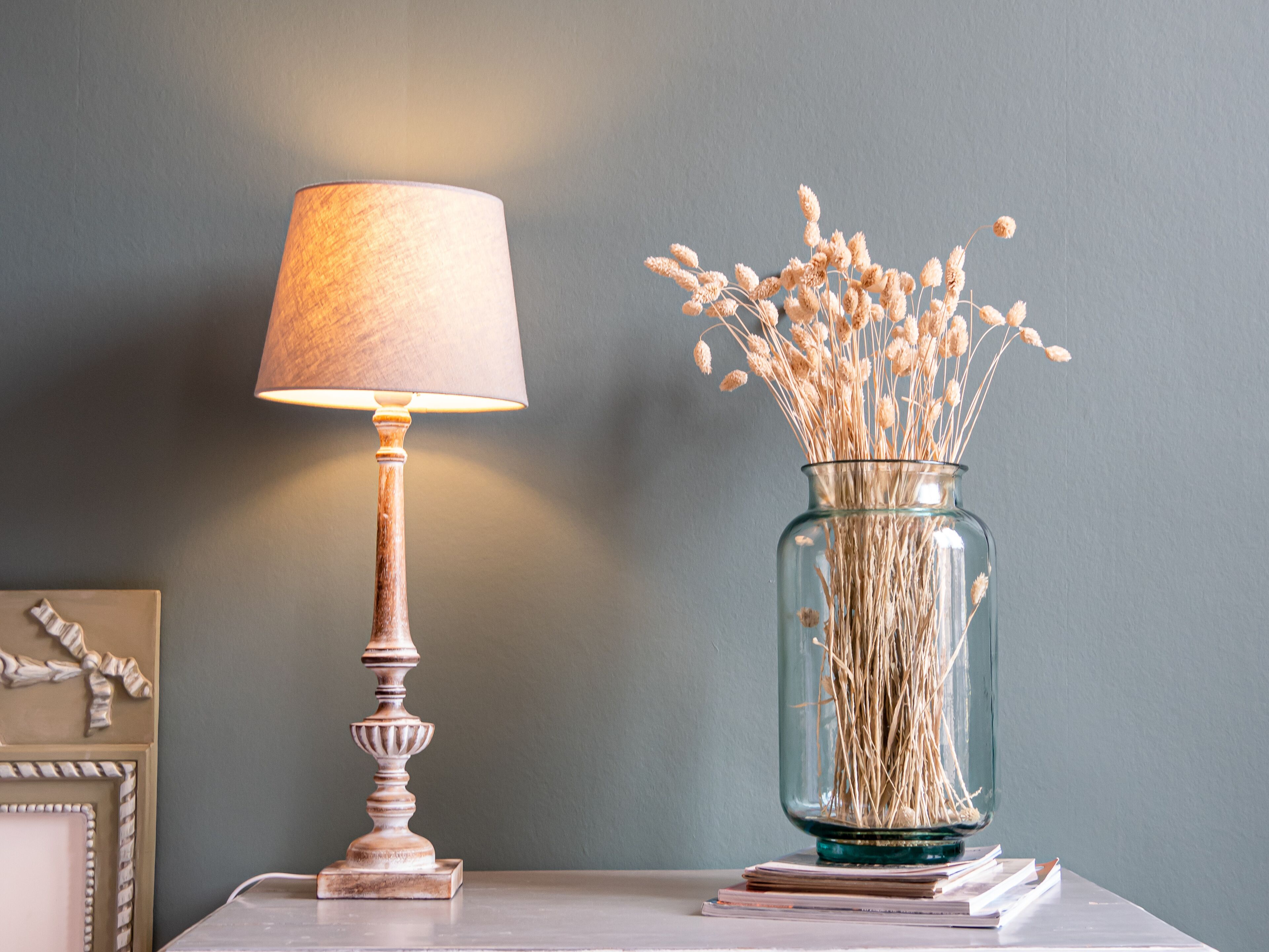 A table with a lamp and a vase of dried flowers.