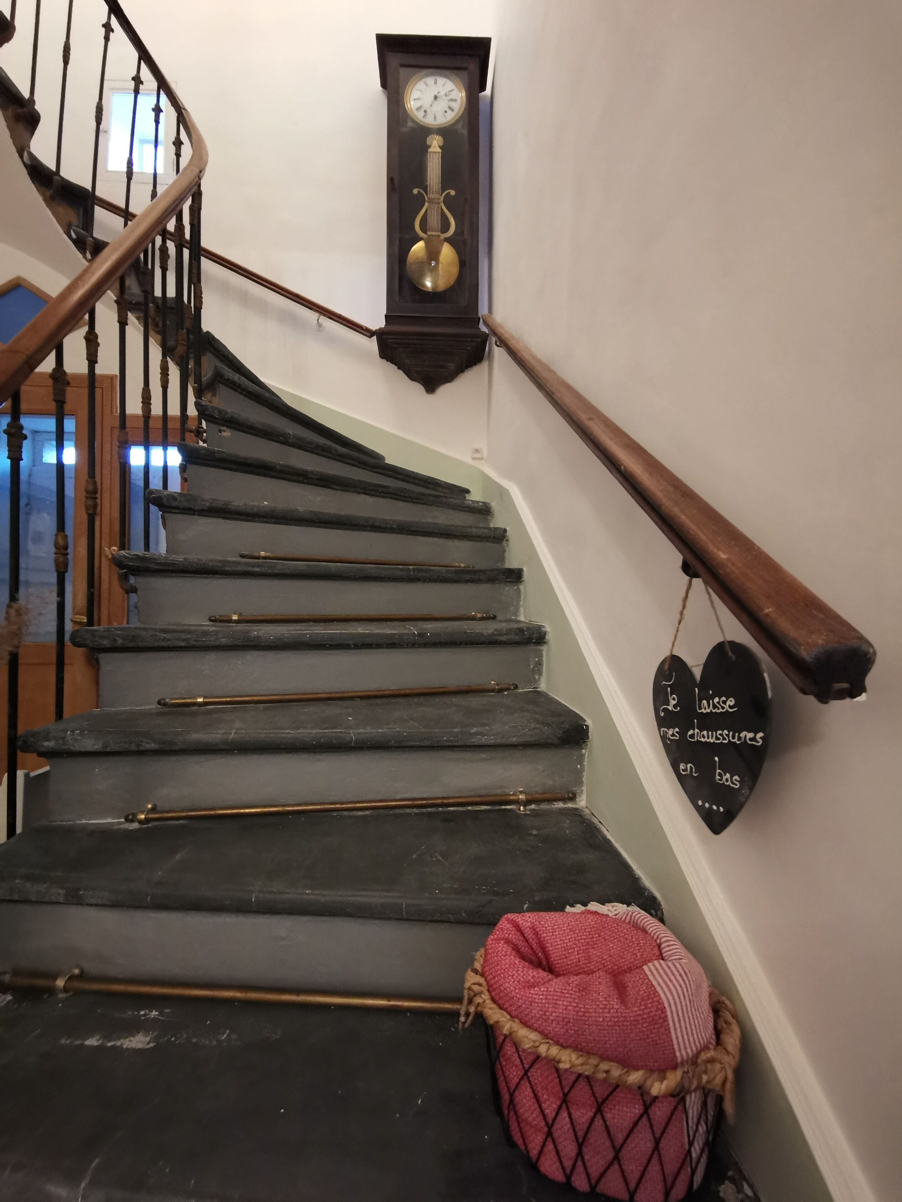 Una escalera con barandilla de madera, un reloj en la pared y un letrero con forma de corazón.