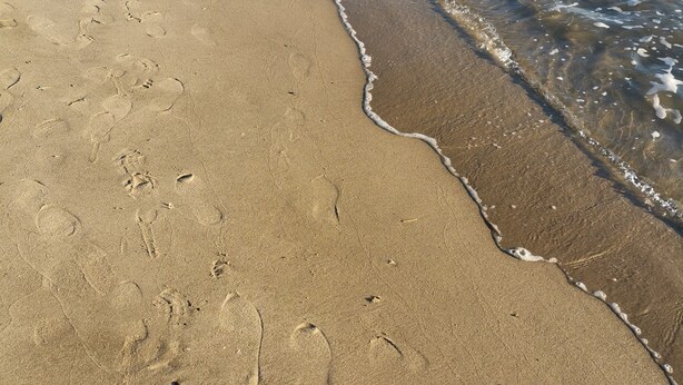 A sandy beach with footprints and a gentle wave.