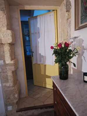 Ein Zimmer mit gelber Tür, weißem Vorhang, einer Blumenvase und einer Marmorplatte.