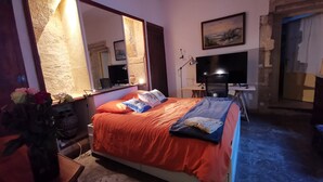 A bedroom with a large bed, a desk with a computer, a TV, and a large mirror.