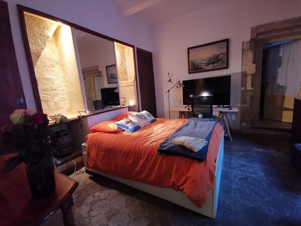 A bedroom with a large bed, a desk with a computer, a TV, and a large mirror.