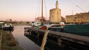 A calm river with boats docked at a pier, a historic tower, and a stone wall in the background.