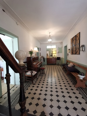 A hallway with a checkered floor, a wooden bench, a piano, and a staircase with a balustrade.