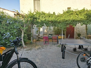 A courtyard with a ping pong table, chairs, a bicycle, and a building with a stone facade.