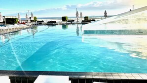 Una piscina con agua cristalina, sillas de descanso, sombrillas y vistas al océano.