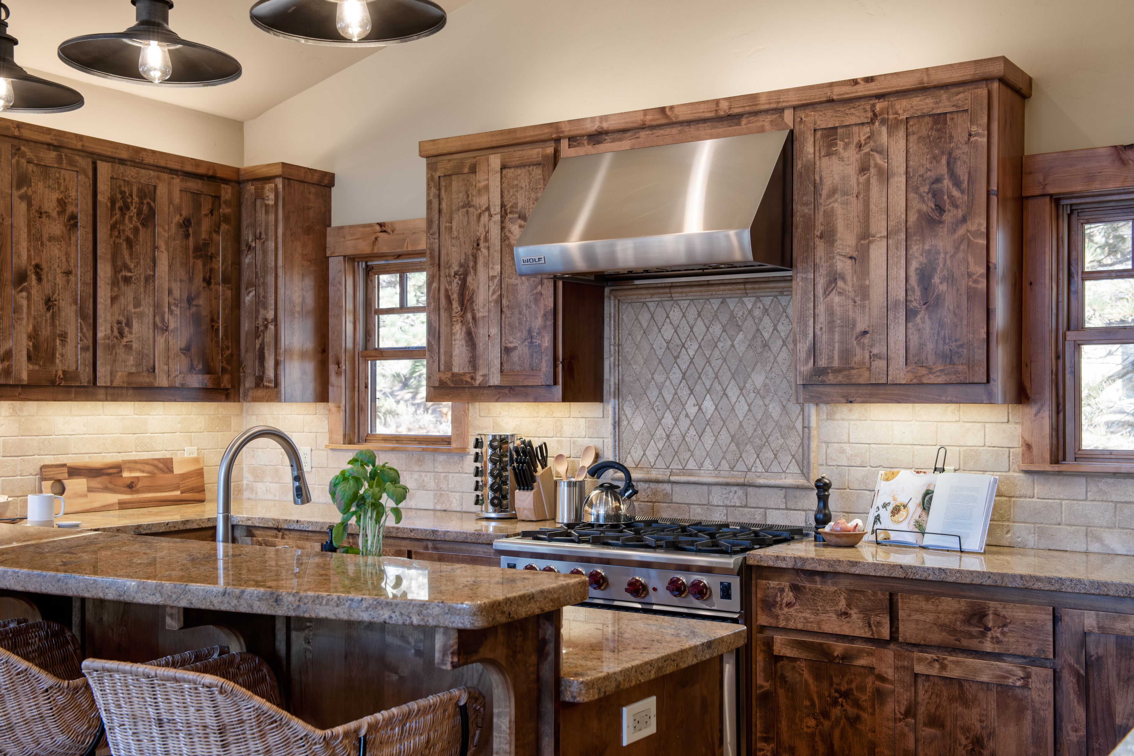 A kitchen with wooden cabinets, a stainless steel range hood, a granite countertop, and a built-in island with seating.