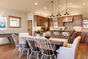Una cocina moderna con armarios de madera, una zona de comedor con sillas blancas e iluminación colgante.