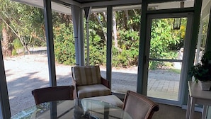 A conservatory with a glass table and two chairs, surrounded by greenery and a gravel path. - Flip Flop 1 (Sanibel)