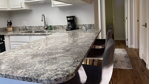A kitchen with a granite countertop, a coffee maker, and a sink. - Flip Flop 1 (Sanibel)