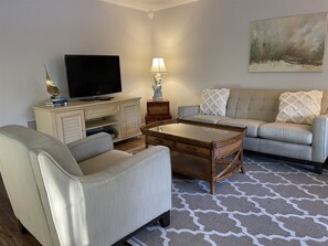 A living room with a sofa, a coffee table, a TV on a cabinet, and a lamp. - Flip Flop 1 (Sanibel)