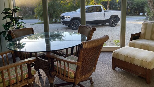 A glass-top dining table with wicker chairs, a cushioned sofa, and a view of a pickup truck outside. - Flip Flop 1 (Sanibel)