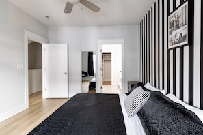 A bedroom with a bed, a ceiling fan, a black and white striped wall, and a door leading to a bathroom.