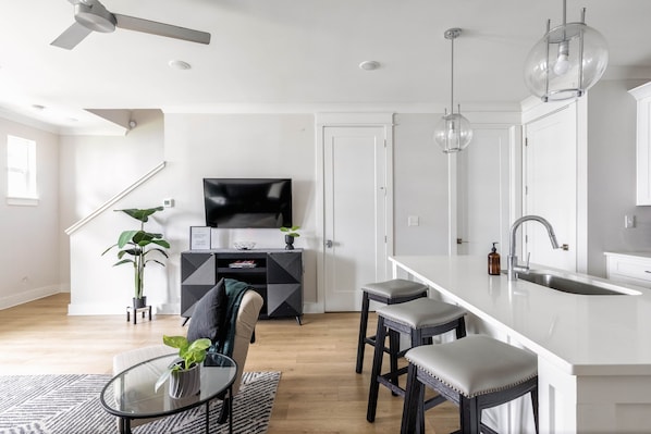 A modern kitchen with a white countertop, bar stools, and a built-in sink.