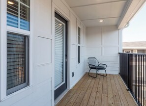 A covered porch with a wooden floor, a metal chair, and a black metal railing.