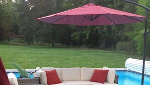 A patio area with a sectional sofa, two side tables, and a red umbrella. - Aux P'tits Bonheurs la Grange (Neuve-Chapelle)