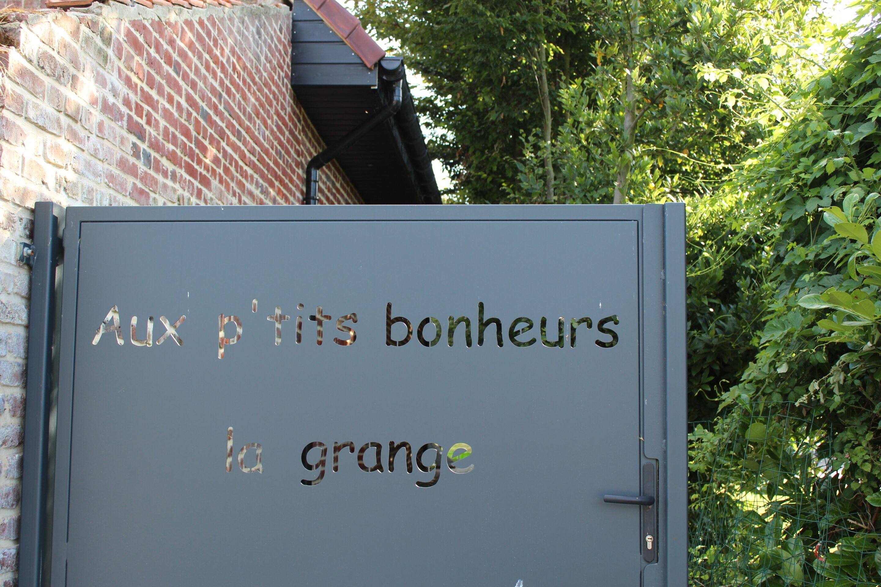 A gray metal door with the text "Aux p'tits bonheurs la grange" in French.