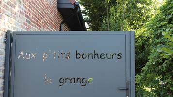 A gray metal door with the text "Aux p'tits bonheurs la grange" in French.