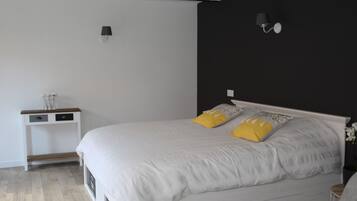 Un dormitorio con una cama blanca, dos almohadas amarillas, una mesita de noche pequeña y una lámpara fijada a la pared.