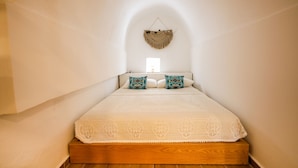 A bedroom with a wooden platform bed, white linens, and two patterned pillows. - Vila Leon - Old Qeparo (Upper Qeparo)