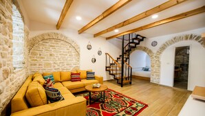 A cozy living room with a stone wall, a wooden staircase, and a sofa with patterned cushions. - Vila Leon - Old Qeparo (Upper Qeparo)