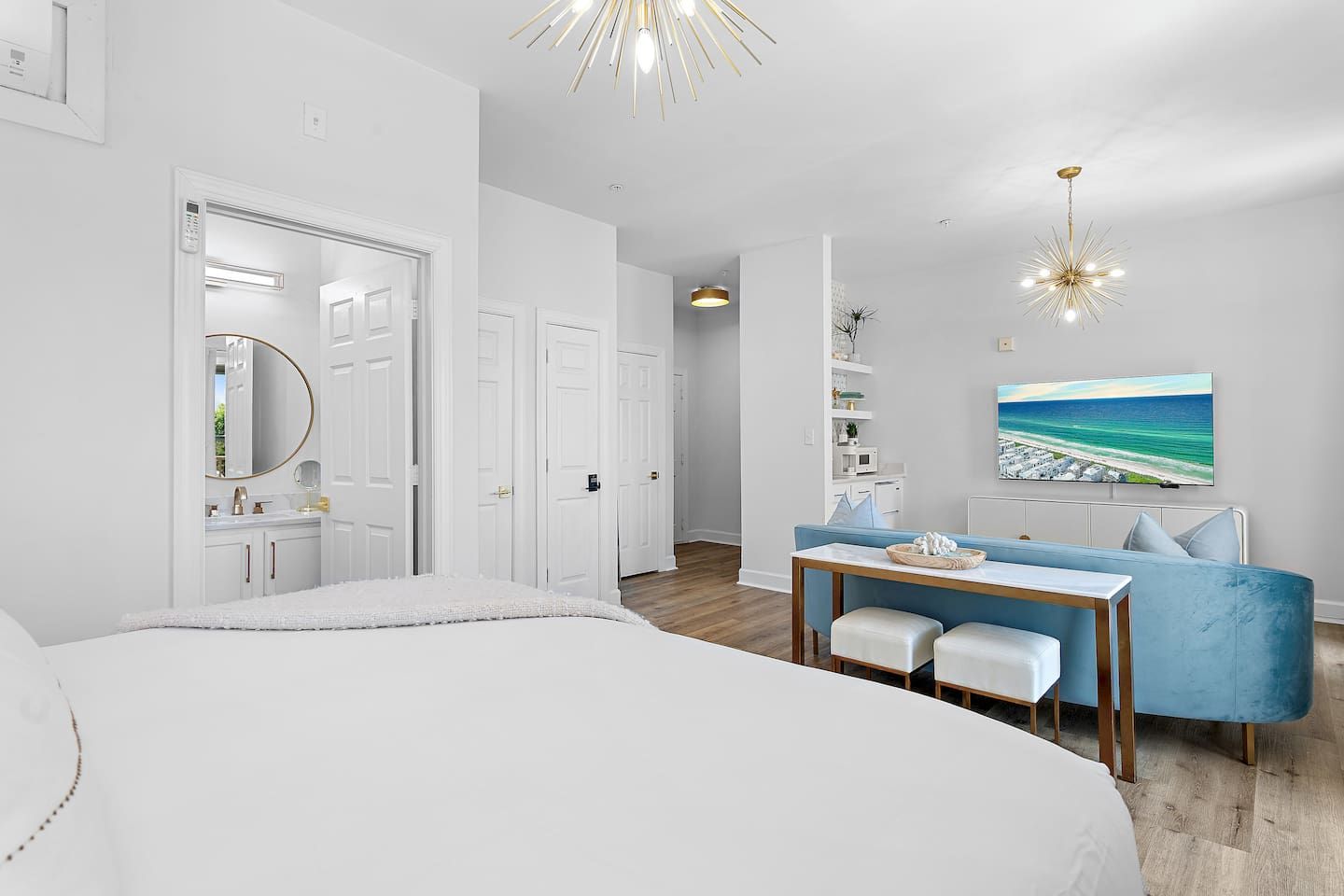 Een moderne slaapkamer met een groot bed, een bureau met stoel, een blauwe bank en een schilderij van een strand.