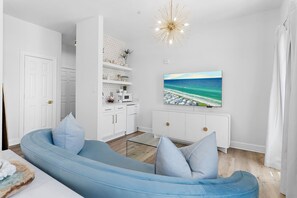 A modern living room with a blue sofa, a flat-screen TV, and a kitchen area with white cabinets.