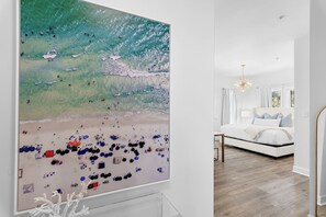 A modern bedroom with a large bed, a chandelier, and a view of the beach.
