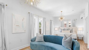 Ein modernes Wohnzimmer mit einem blauen Sofa, einem Bett mit weißer Bettwäsche und einem Glastisch.